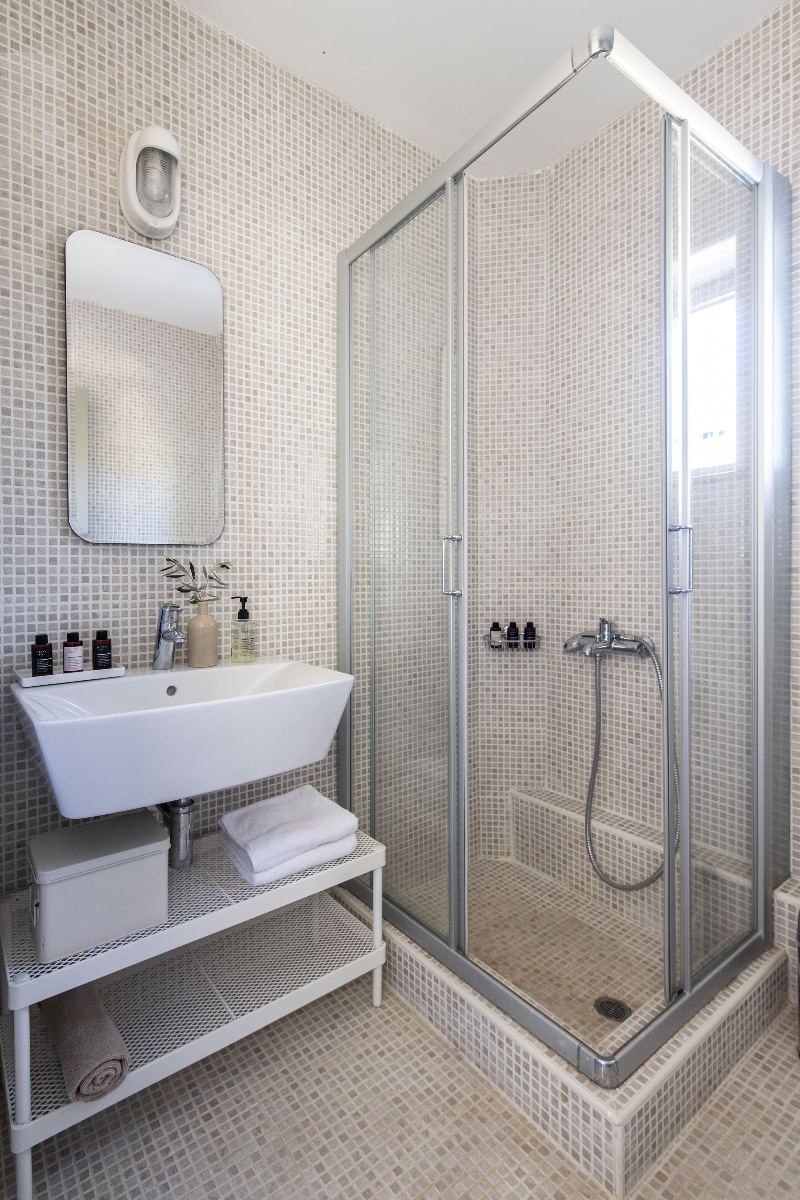 Un baño moderno con ducha envuelta en vidrio, un lavamanos blanco y un espejo sobre él.