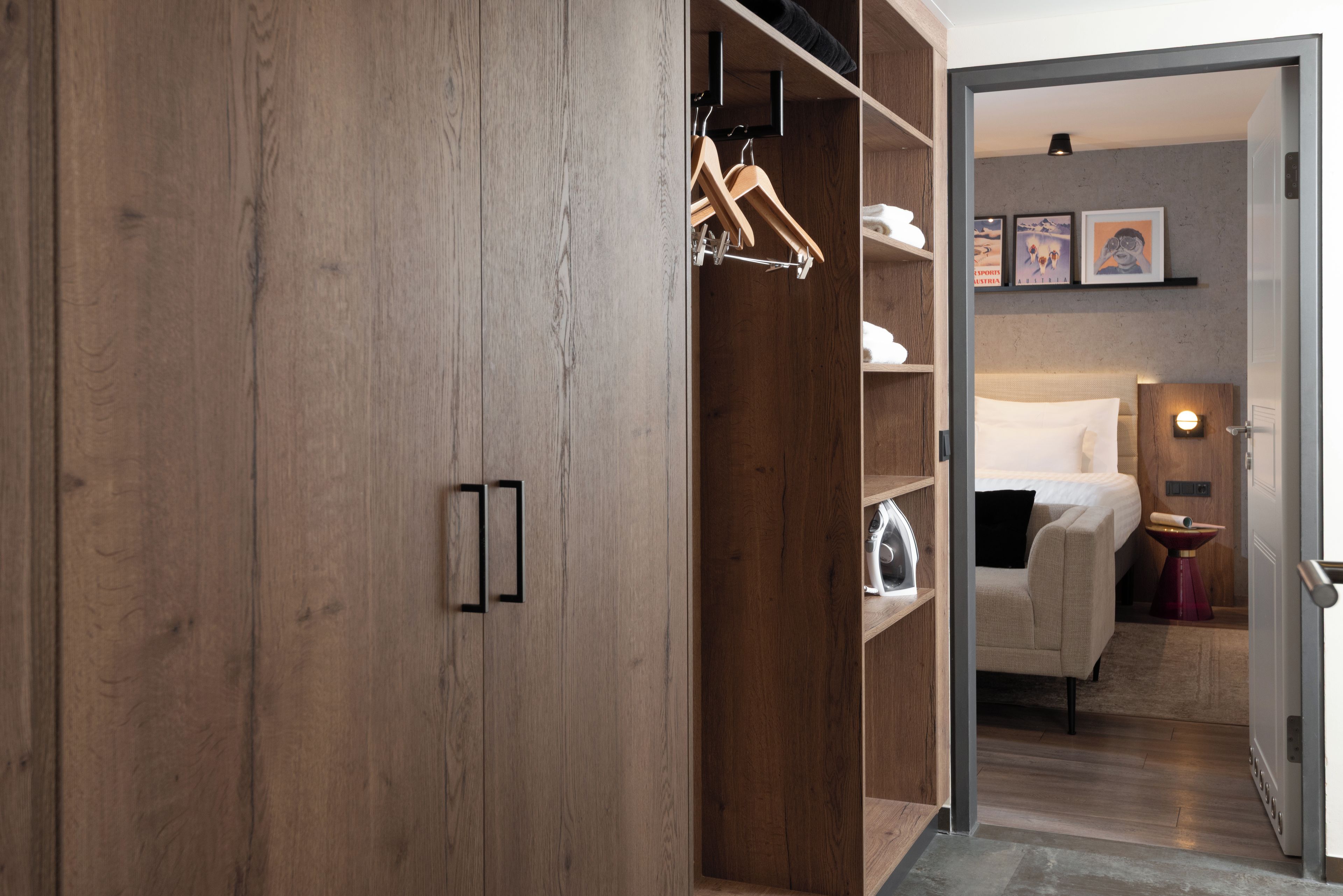 Une chambre d’hôtel avec une armoire en bois, un lit, une table de chevet et un mur orné de tableaux encadrés.