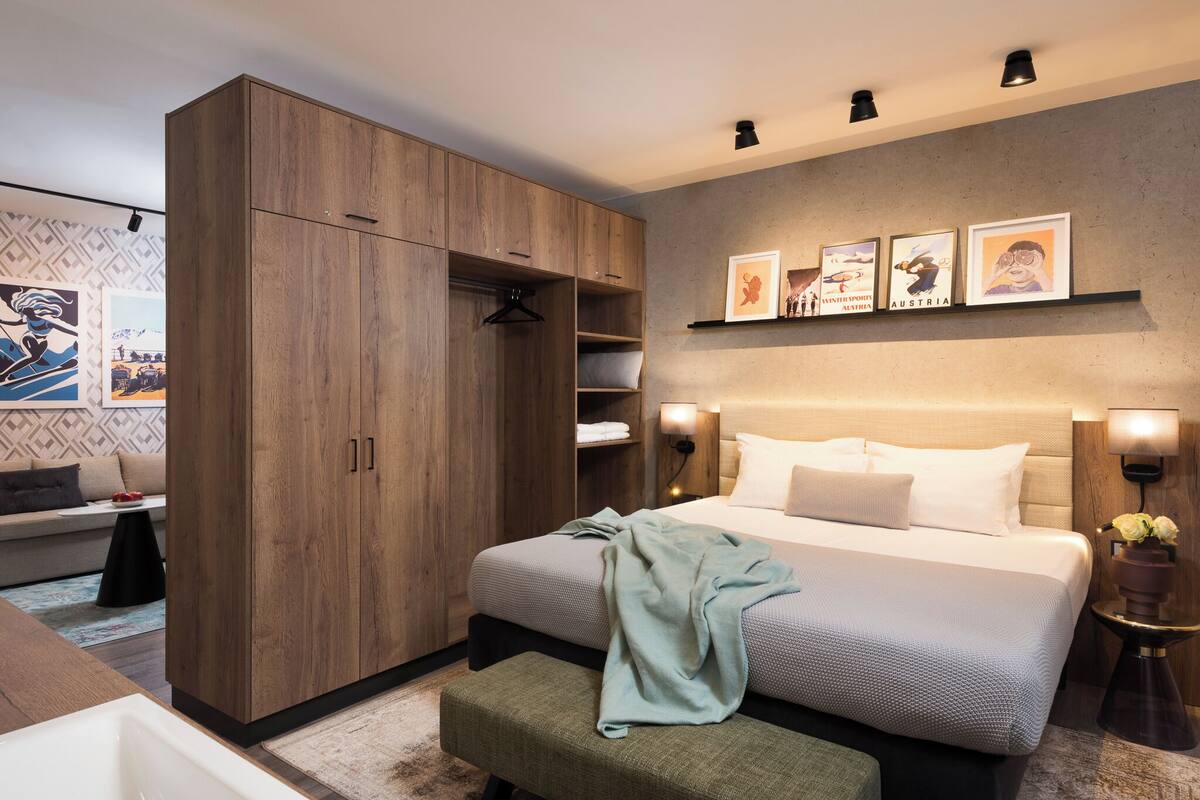 A modern bedroom with a large bed, wooden wardrobe, and a bedside table with a lamp.