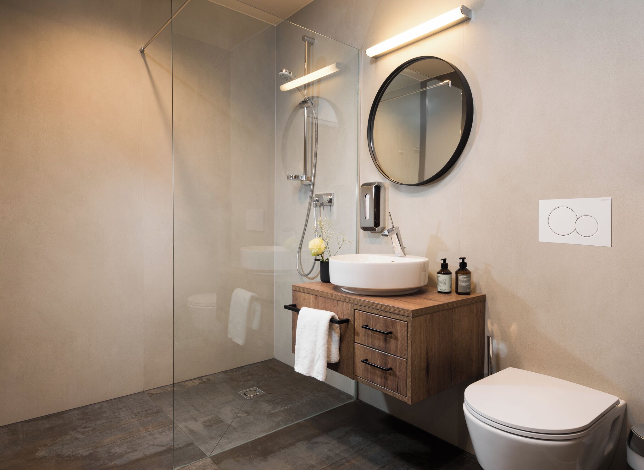 A modern bathroom with a glass shower enclosure, a wooden vanity with a sink, and a toilet.