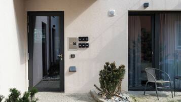 A building entrance with a glass door, a small potted plant, a chair, and a stone pathway.