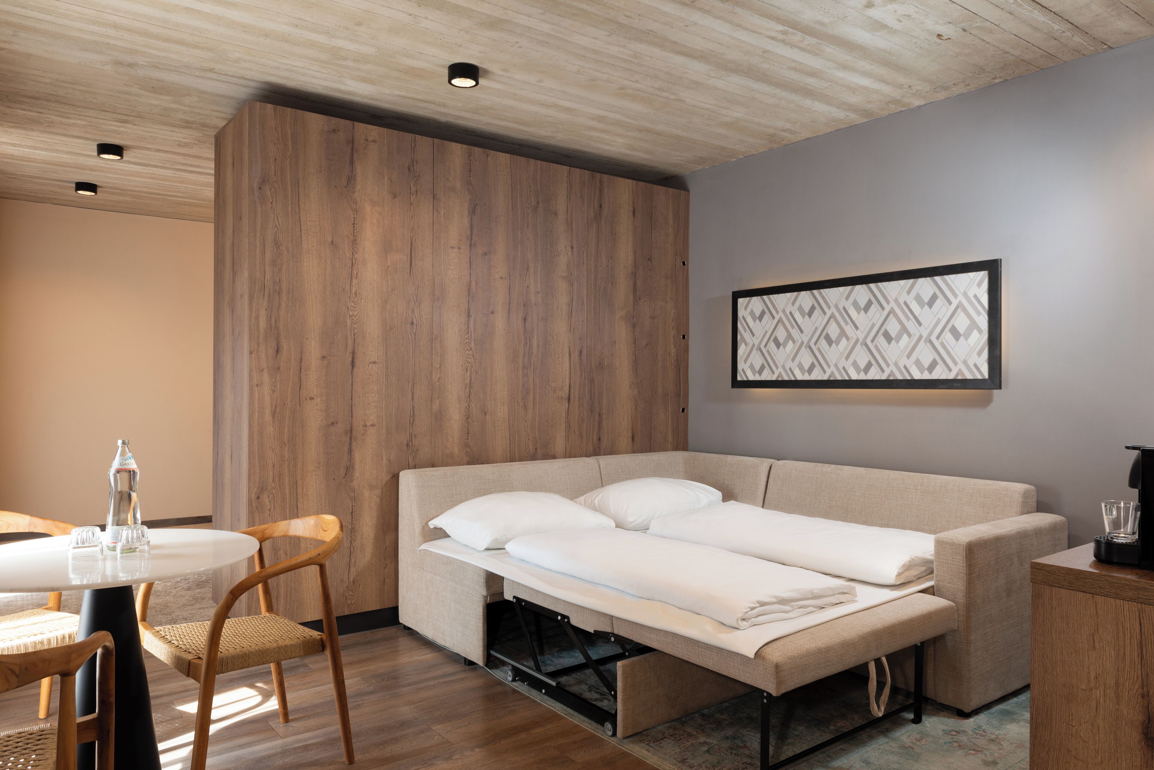 A compact room with a sofa bed, a dining table with chairs, and a wall-mounted artwork.