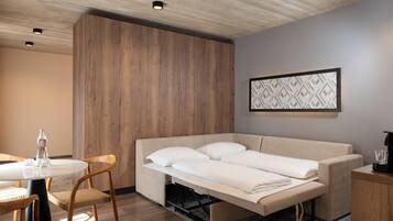 A compact room with a sofa bed, a dining table with chairs, and a wall-mounted artwork.