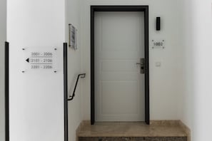 Una puerta blanca con marco negro, un buzón negro pequeño y un cartel fijado a la pared con números de habitación.