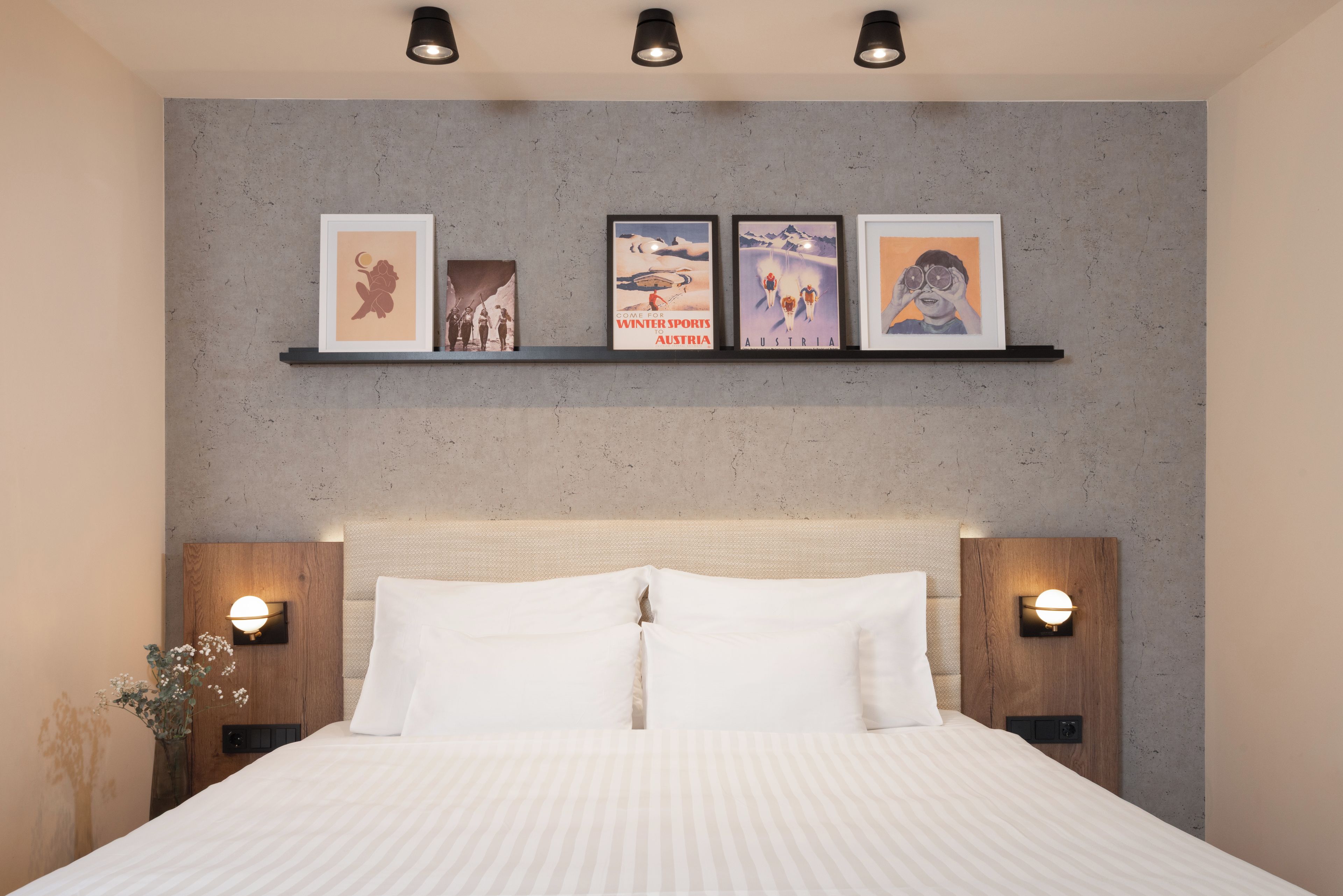 A bedroom with a bed, headboard, bedside tables, and wall-mounted picture frames.