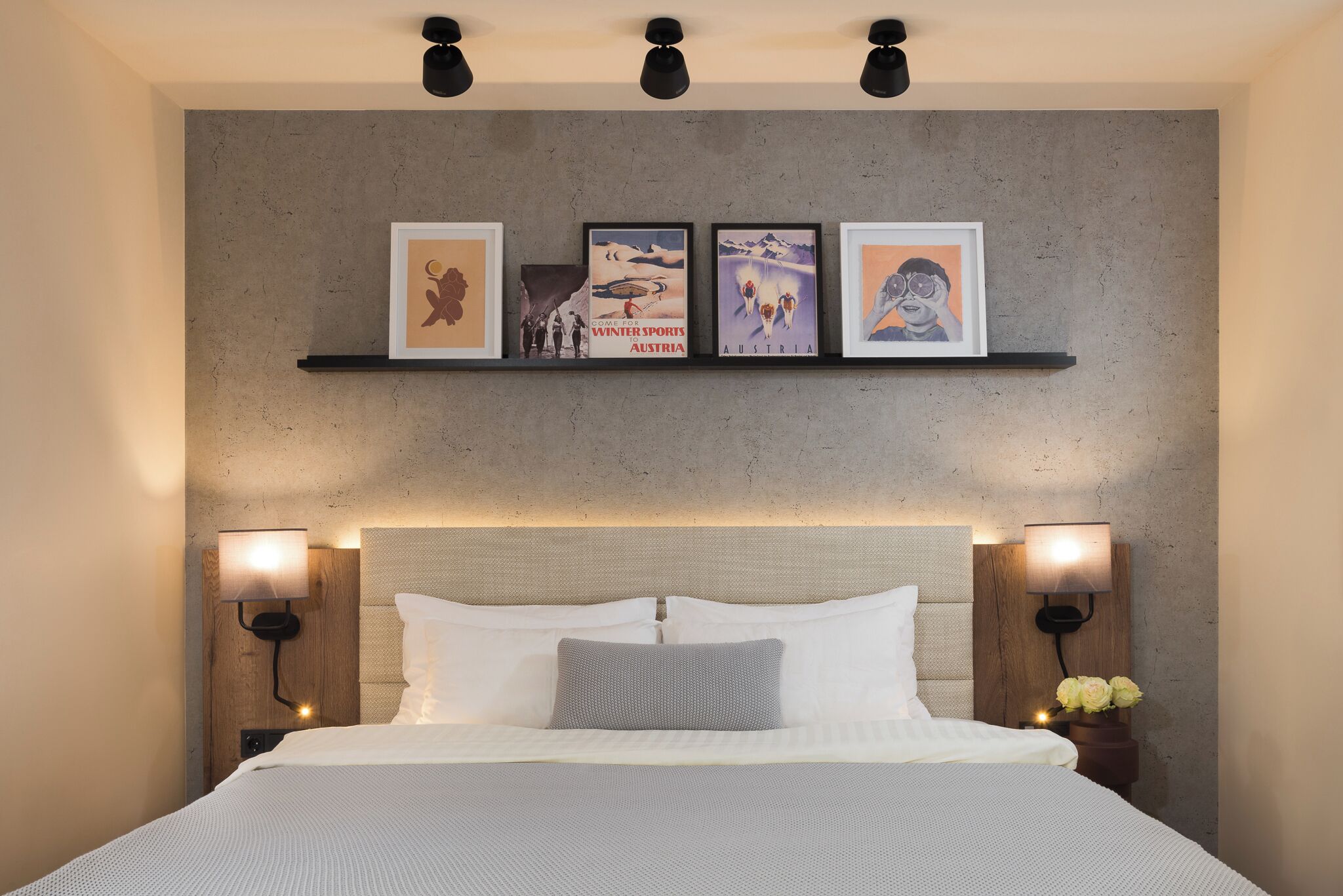 A neatly arranged bedroom with a bed, two bedside tables, and a wall-mounted shelf with framed pictures.