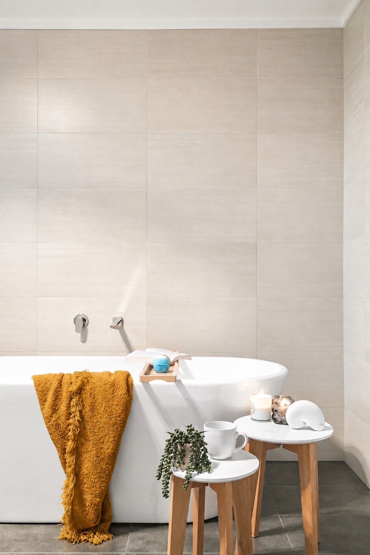 Une salle de bain moderne avec une baignoire, un petit tabouret en bois, une table blanche et une serviette jaune.