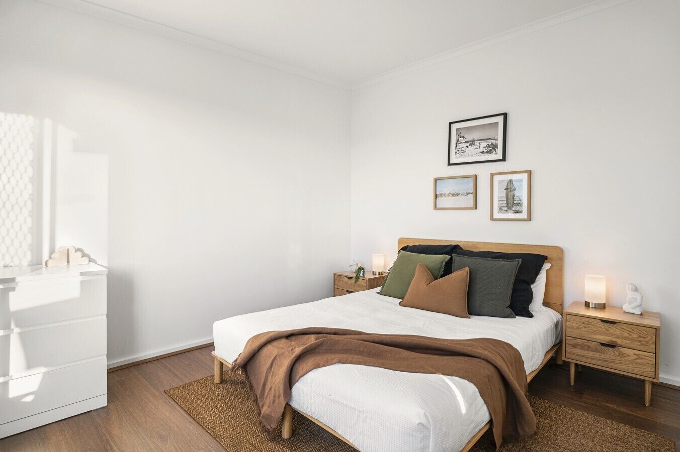A bedroom with a bed, bedside tables, a nightstand, a dresser, and wall-mounted pictures.
