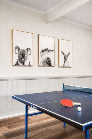 Ein Tischtennistisch mit einem roten Schläger und einem Ball, ein blauer Tischerahmen und drei gerahmte Tierbilder an der Wand.