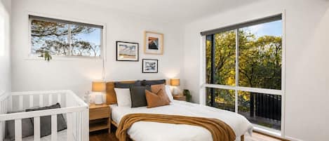 A bedroom with a large window, a crib, and a bed with a headboard.