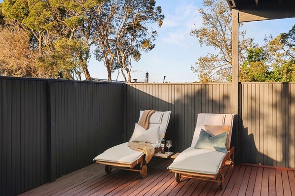 A deck with two sun loungers, a bottle, and a glass.