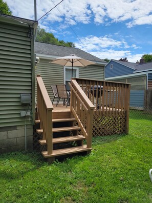 Een houten terras met een balustrade, een patio tafel en een stoel, grenzend aan een huis met een garage.