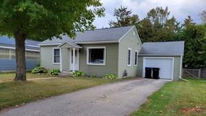 A two-story house with a gravel driveway leading to a garage. - Dog-Friendly, Fenced-In Backyard, Quiet Neighborhood (Sturgeon Bay)