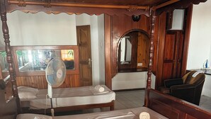A wooden four-poster bed with white linens and pillows, a standing fan, and a mirror above the bed. - Diamond Plaza Beachfront Apartment  (Grand Anse)