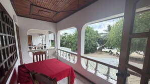 A room with a red table, wooden chairs, a white ceiling, and large windows overlooking a beach. - Diamond Plaza Beachfront Apartment  (Grand Anse)