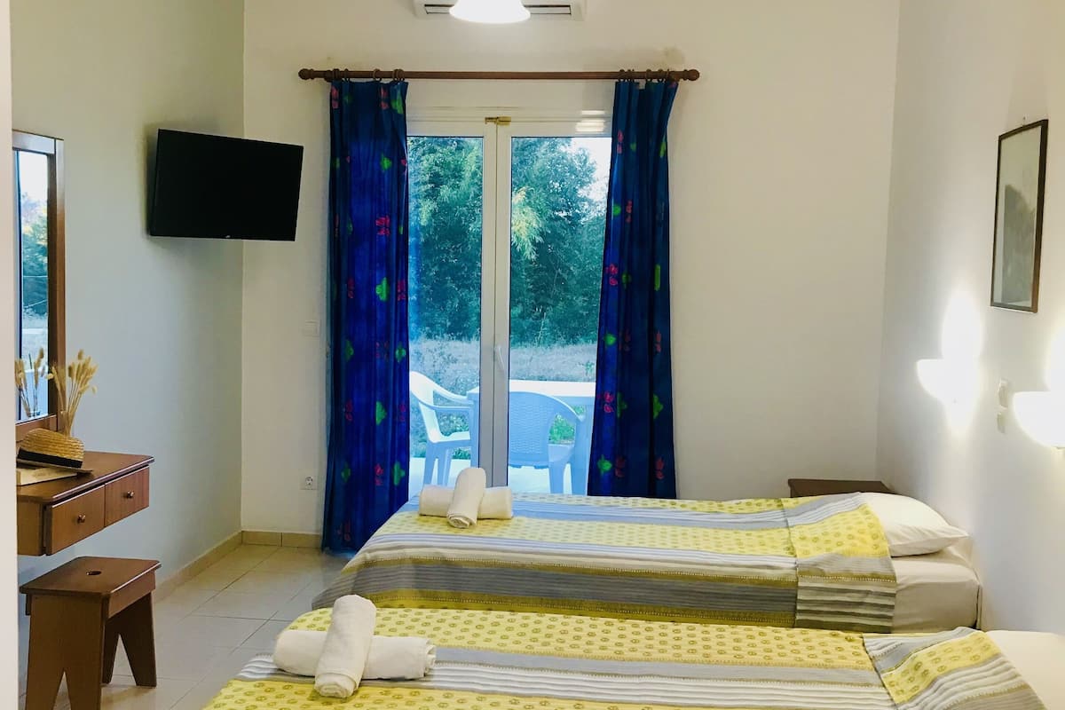 A hotel room with two beds, a desk, a TV, and a window with curtains.