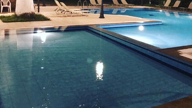 A swimming pool at night with lounge chairs and a palm tree. - Banos apartments and swimming  pool (Corfu)