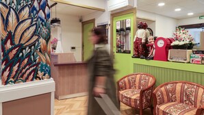 A reception area with a green wall, a clock, and floral decorations. - Hôtel GLORIA (Grenoble)