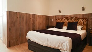 A bedroom with a wooden headboard, a large bed with white and dark bedding, and a nightstand with a lamp. - Hôtel GLORIA (Grenoble)