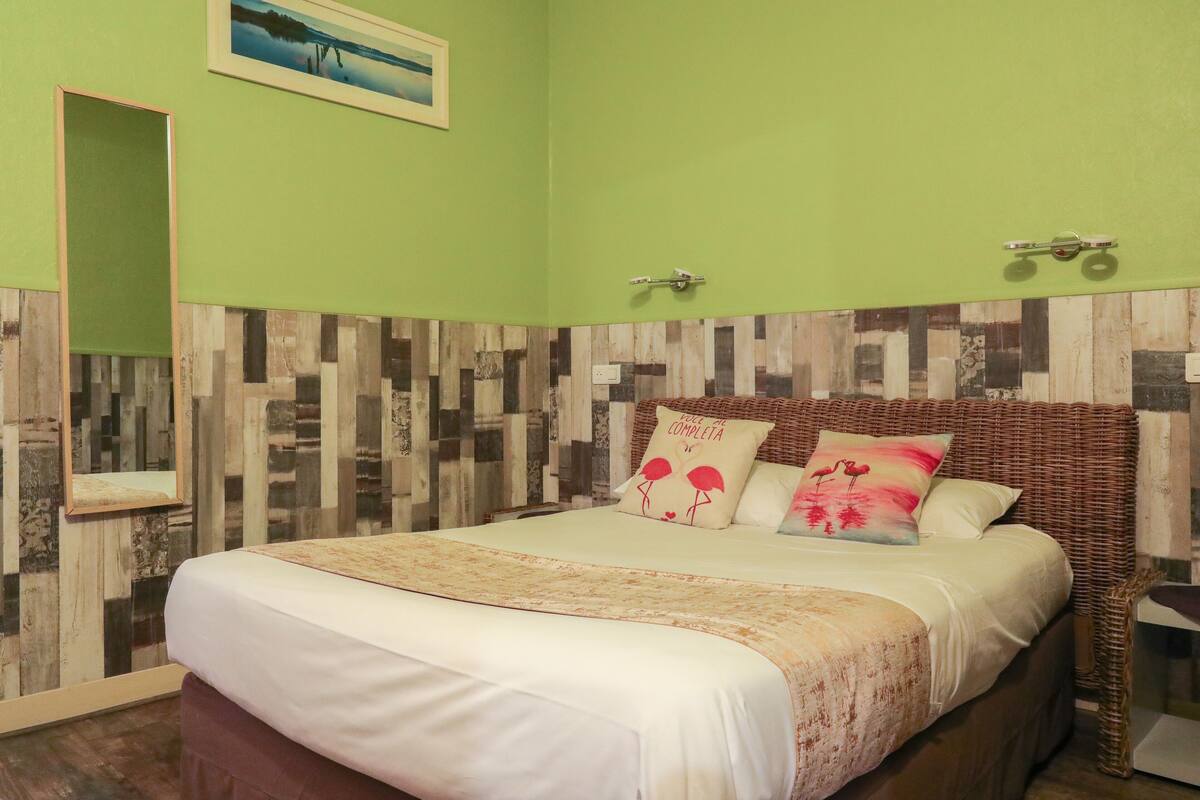 Una cama bien hecha con una colcha estampada con motivos florales, un espejo y una pared con un diseño de madera.