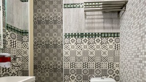 A bathroom with patterned tiles, a white toilet, a shower area, and a sink with a mirror. - Hôtel GLORIA (Grenoble)