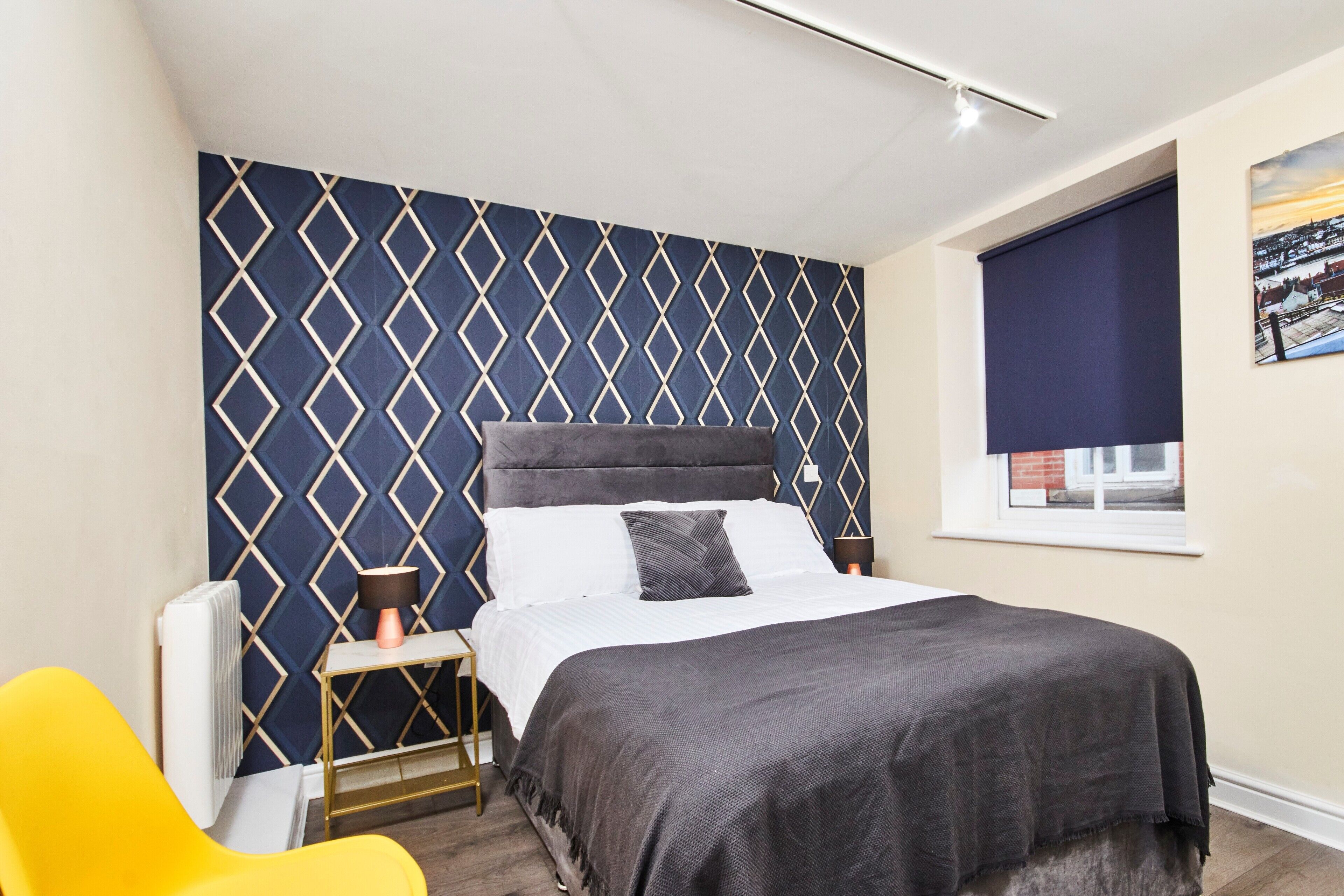 A bedroom with a bed, a bedside table, a lamp, a chair, and a window with a view.