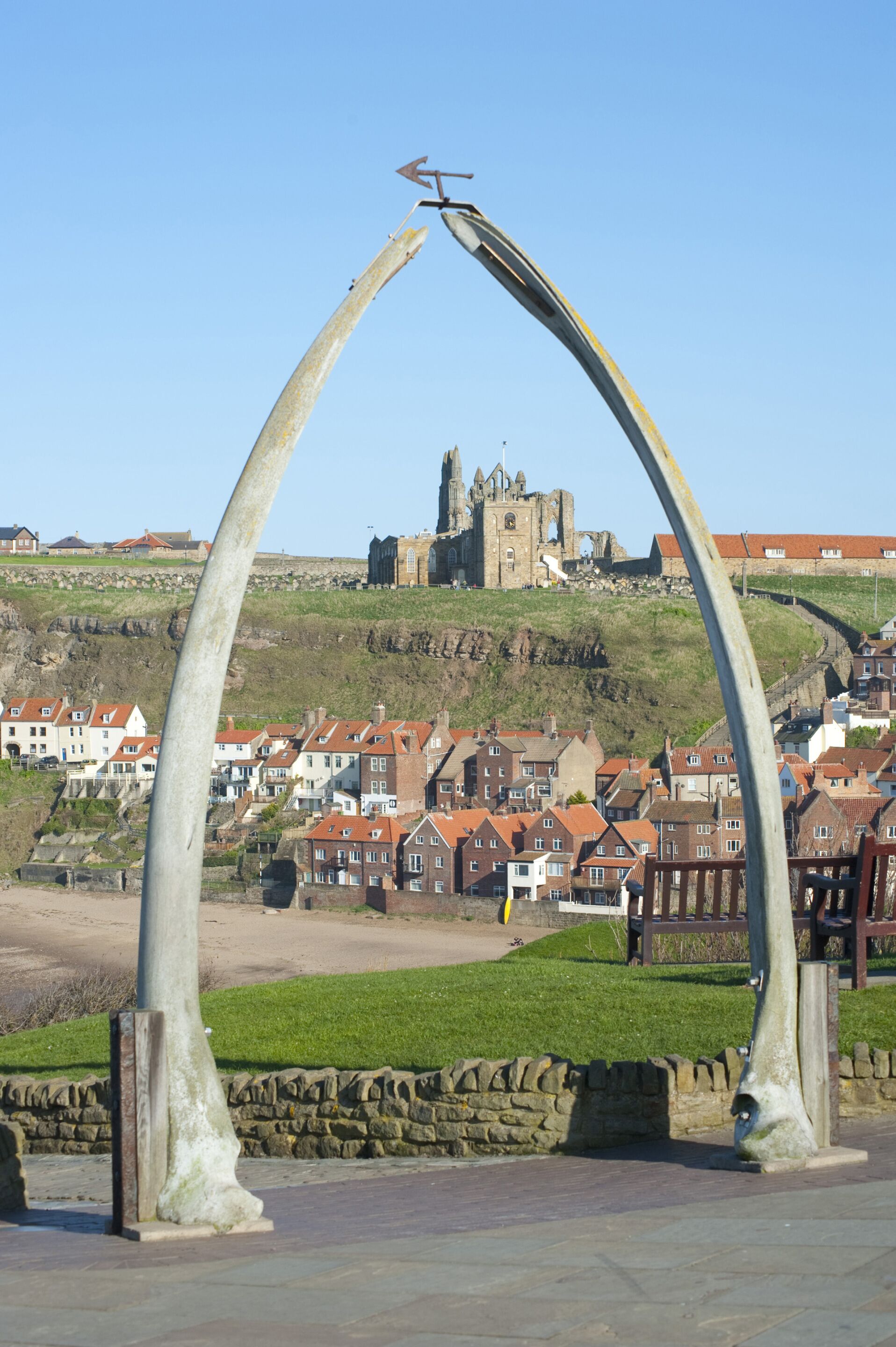 A historic building with a clock tower, surrounded by residential houses and a large sculpture in the foreground.