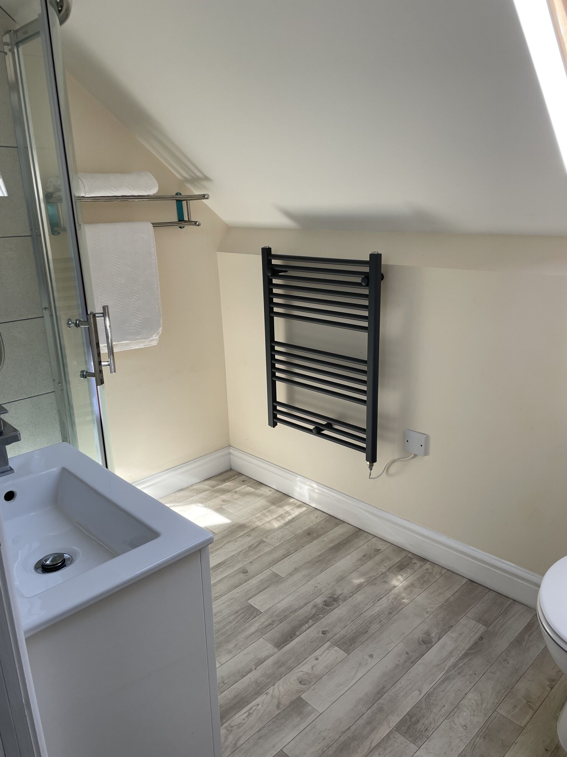 A bathroom with a white sink, a glass shower enclosure, a black towel rack, and a wooden floor.