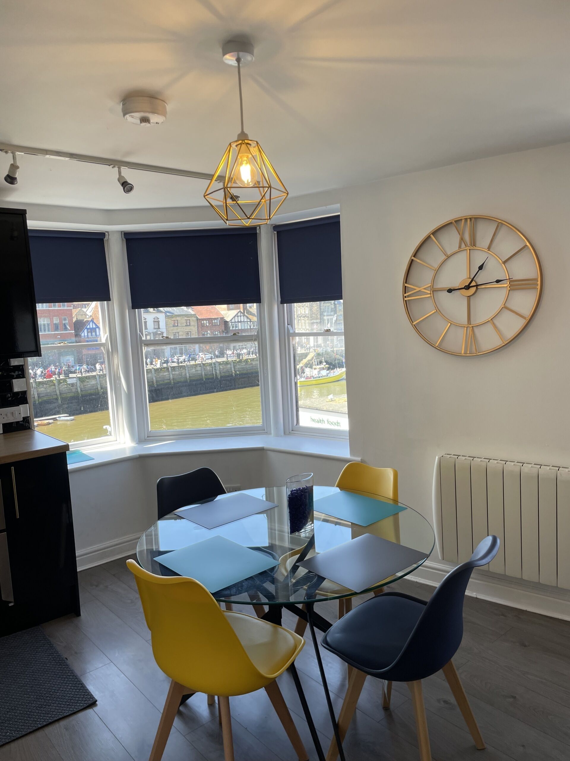 A dining area with a round table, chairs, a clock, and a view of the outside.