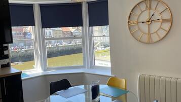 A dining area with a round table, chairs, a clock, and a view of the outside.