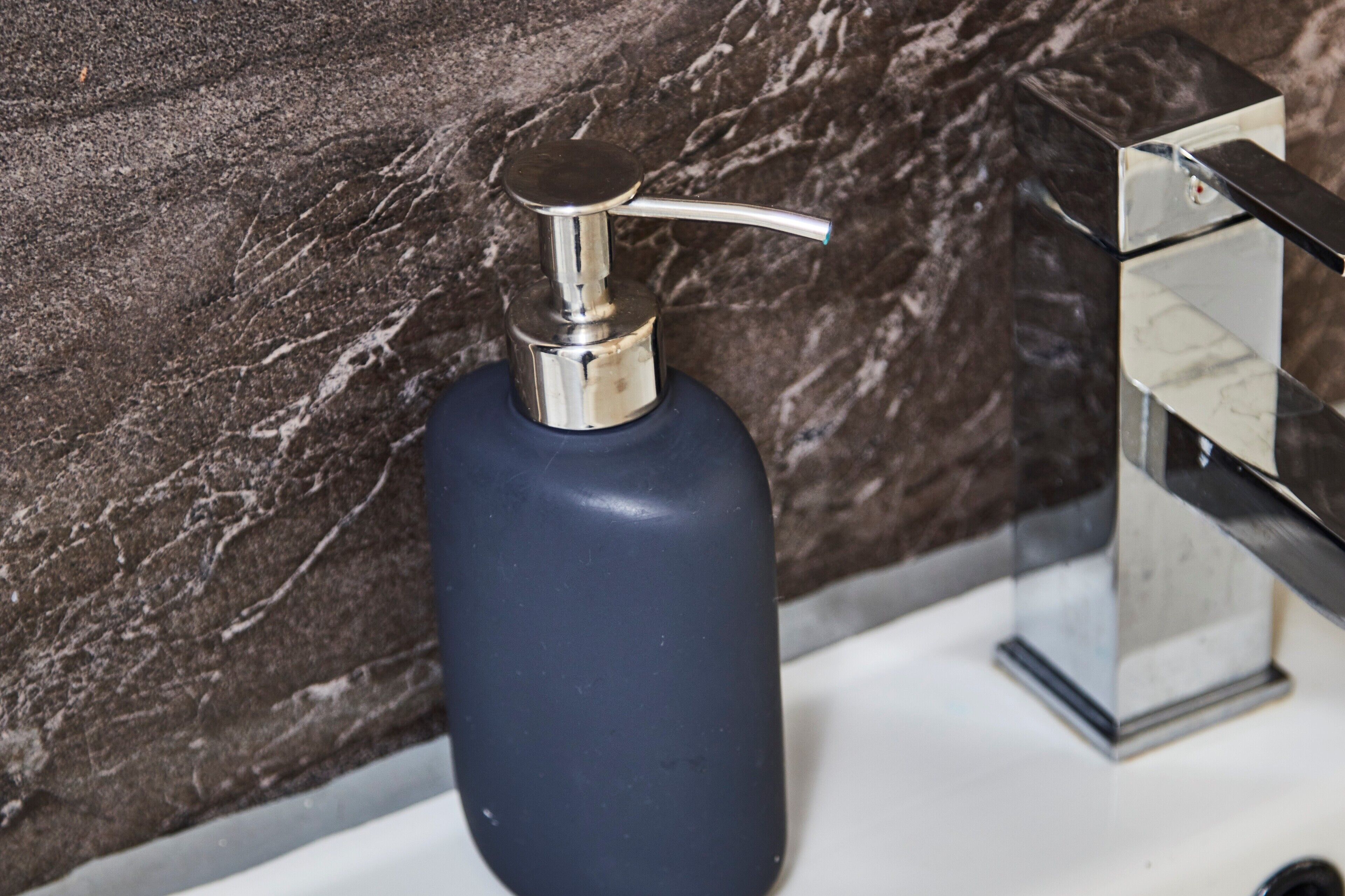 A bathroom with a marble wall, a blue soap dispenser, and a chrome faucet.