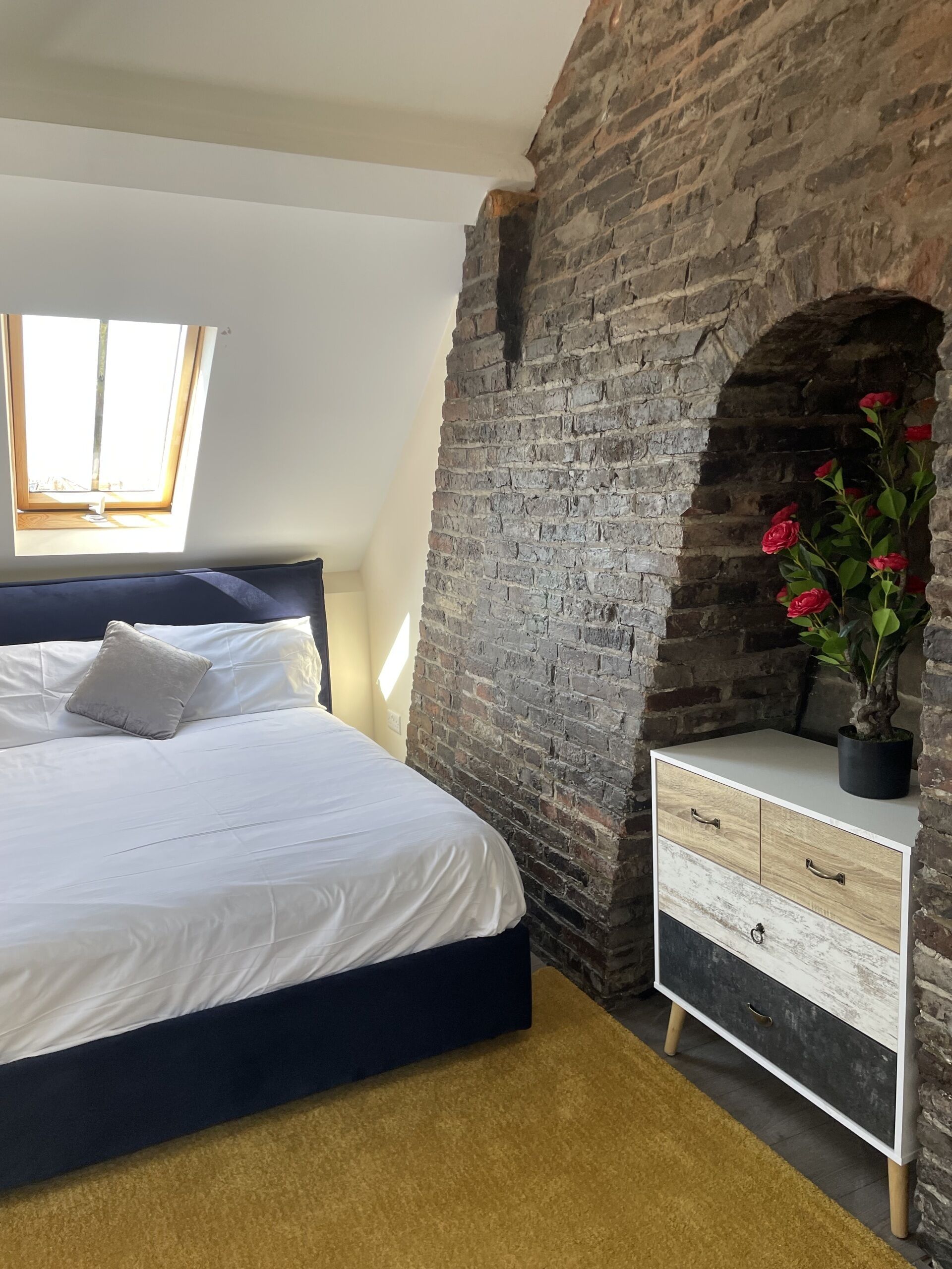 A bedroom with a bed, a dresser, a brick wall, and a skylight.