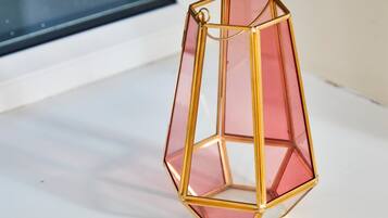 A hexagonal, gold-framed, pink-tinted lantern hanging by a window.