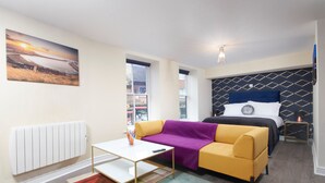 A modern bedroom with a bed, a sofa, a small table, and a painting of a sunset. - Whitby Bridge Luxury Apartments (Whitby)