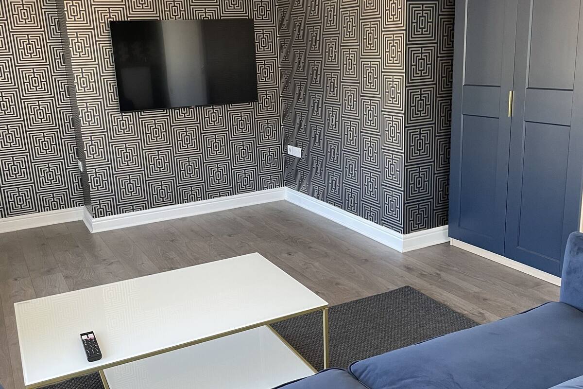 A modern living room with a blue sofa, a white coffee table, and a flat-screen TV mounted on the wall.