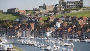 A harbor with numerous boats docked, surrounded by traditional buildings with red roofs and a historic castle in the background. - Whitby Bridge Luxury Apartments (Whitby)