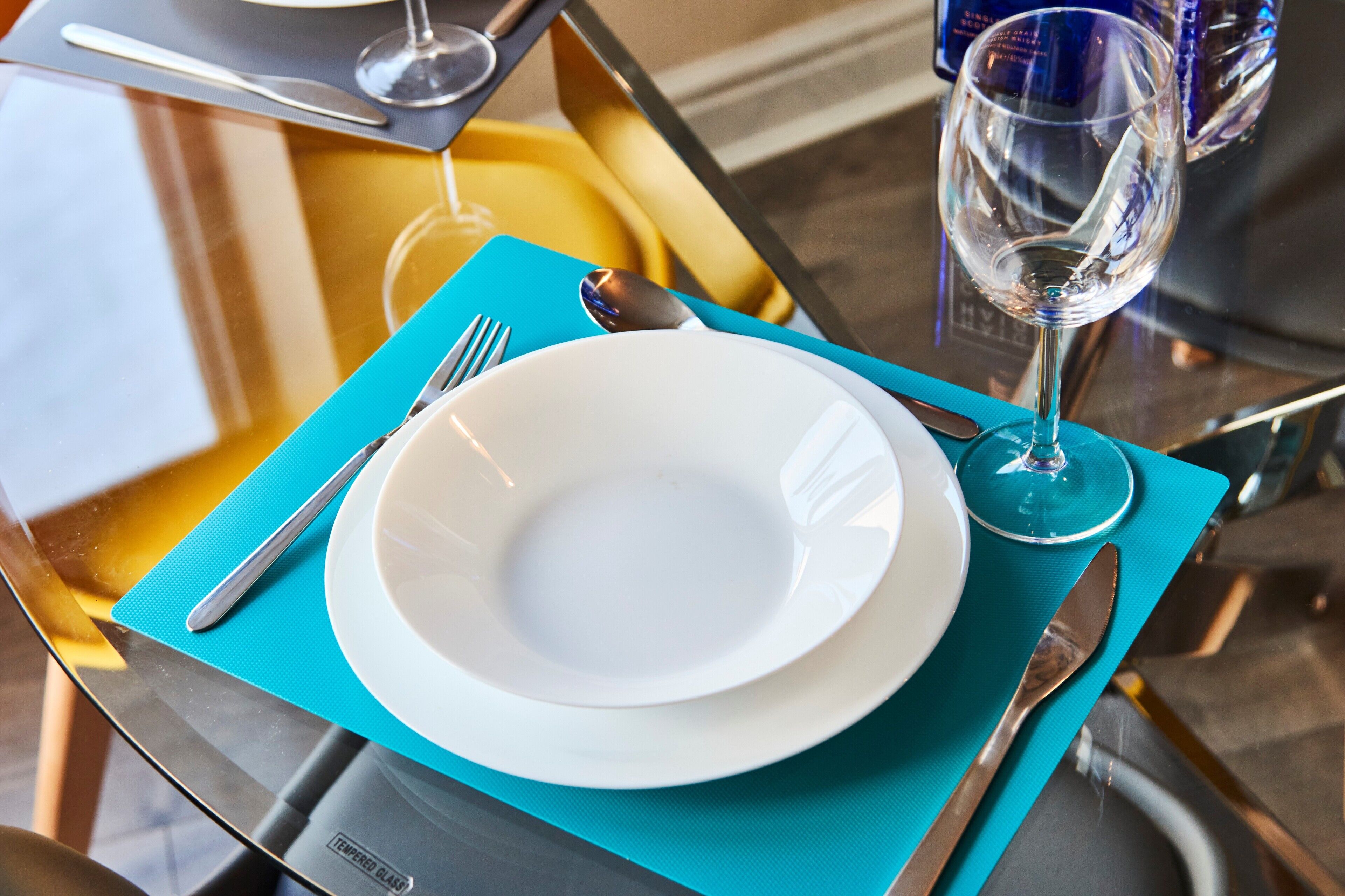 A table set with a white plate, a fork, a knife, and a glass of water on a blue placemat.
