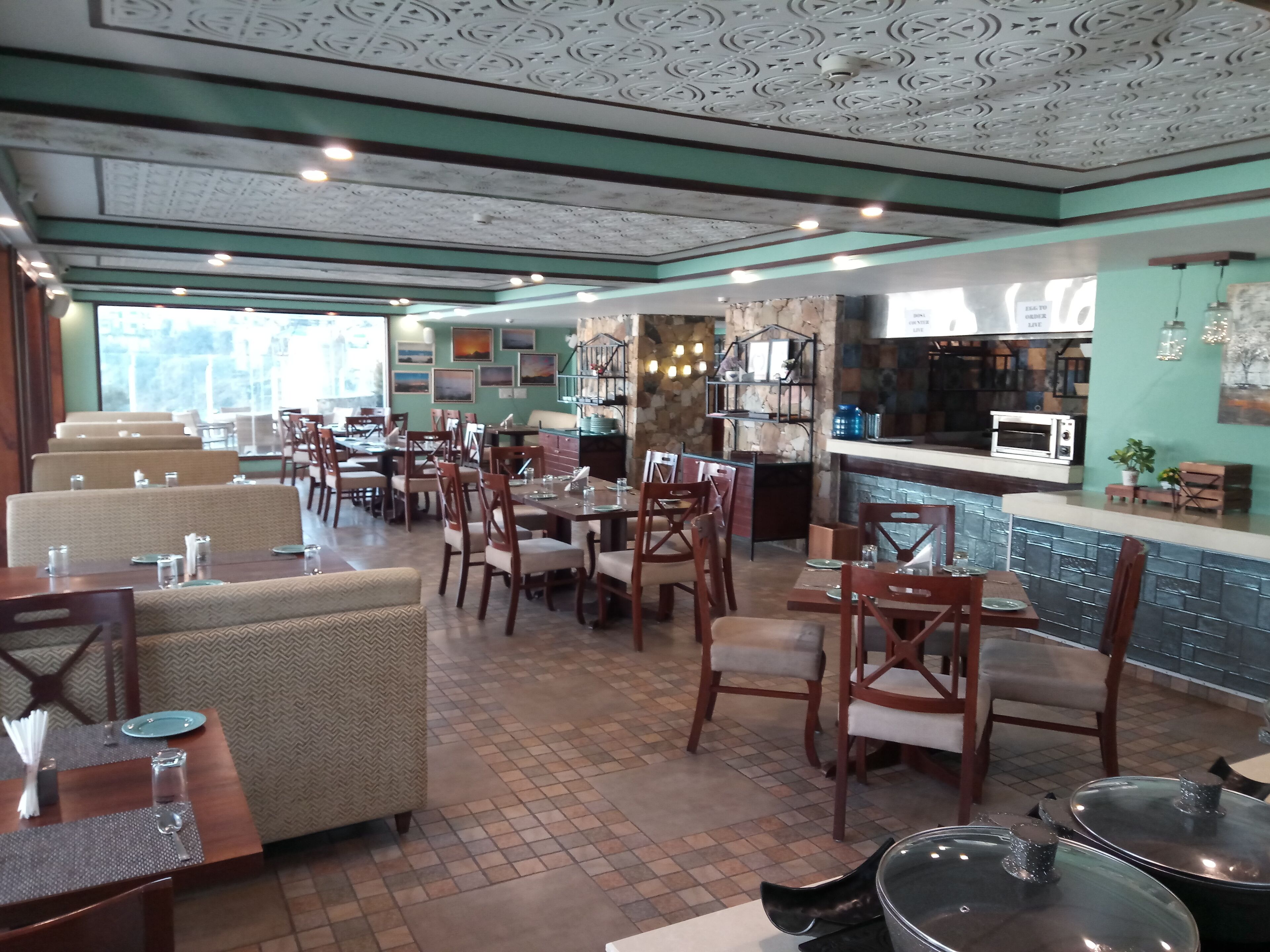 A restaurant with multiple dining tables and chairs, a bar area, and a stone wall with artwork.