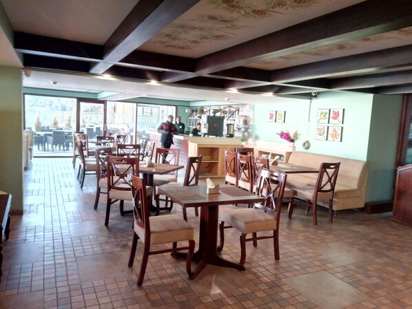 An indoor dining area with wooden tables and chairs, a counter with staff, and a view through large windows.