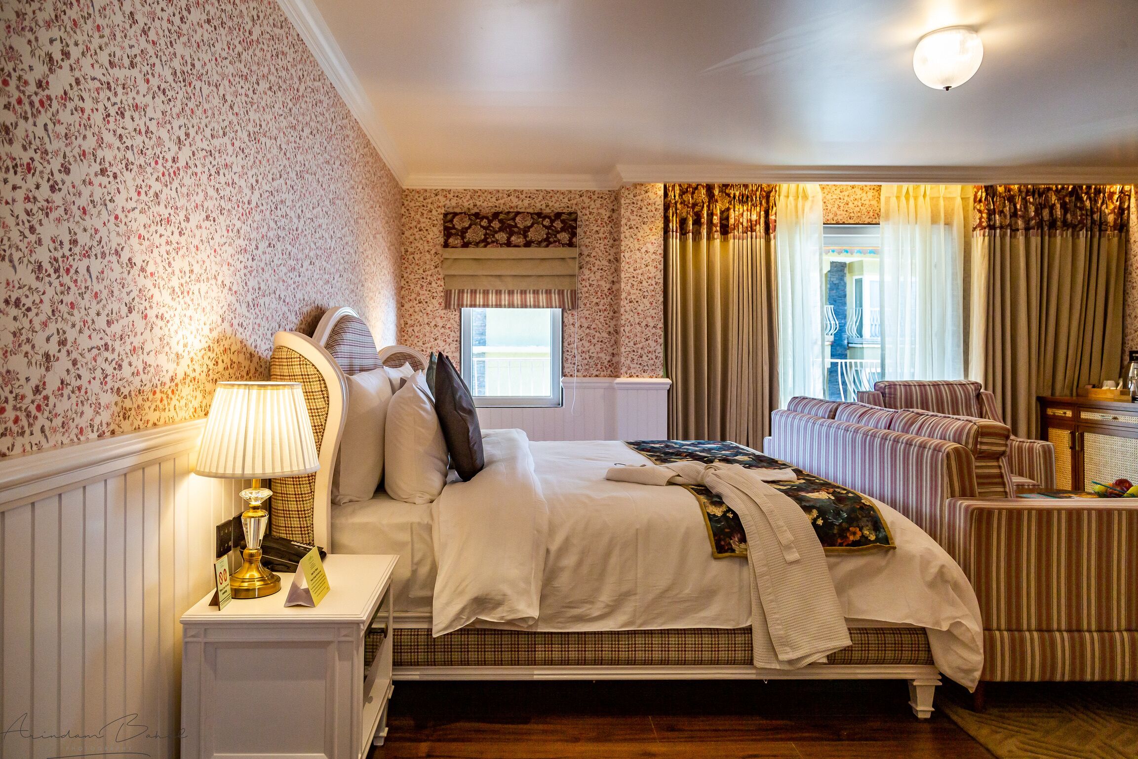 Une chambre à coucher bien rangée, avec un lit, des tables de chevet, une lampe, une fenêtre avec des rideaux et une vue sur l’extérieur.