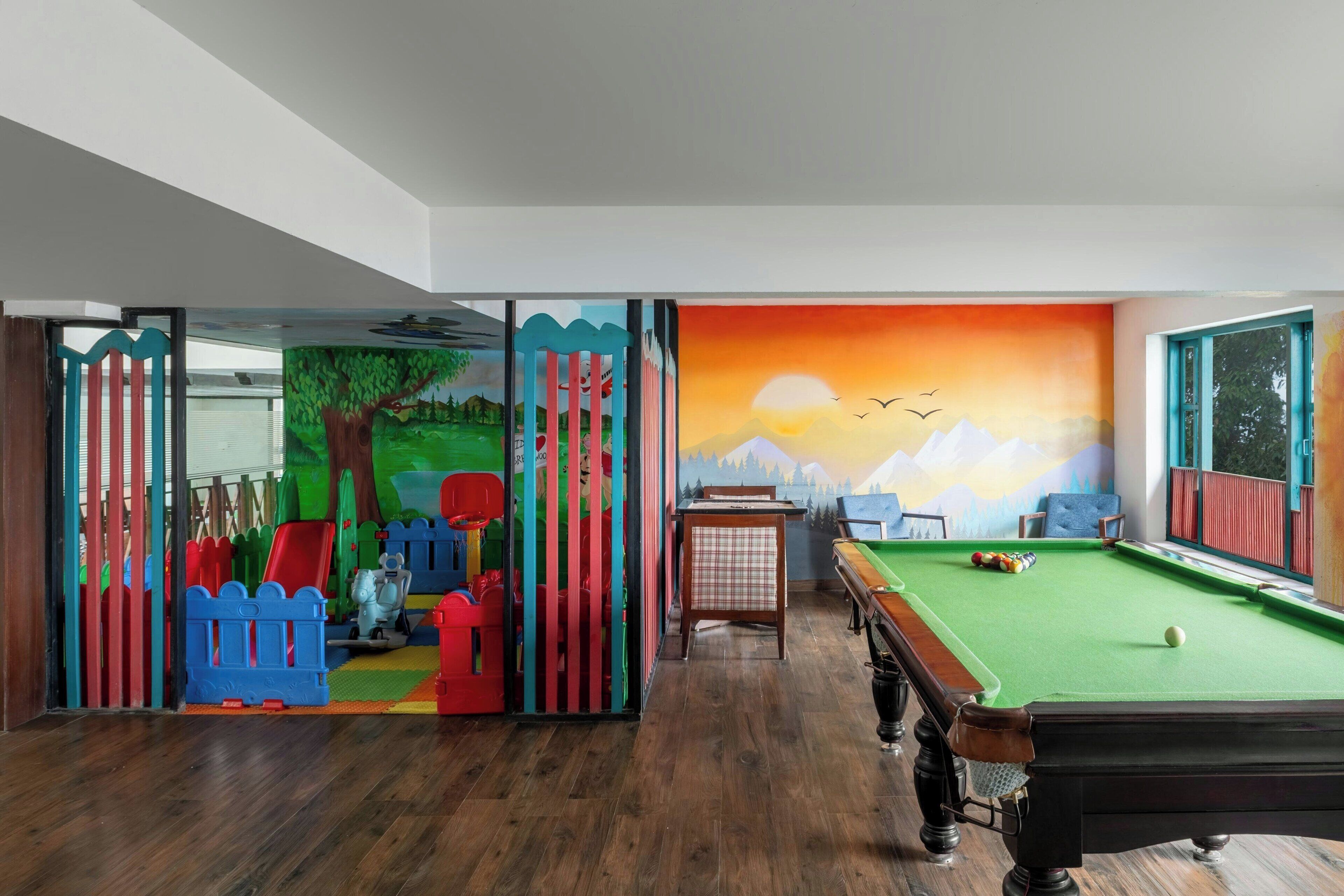 A room with a pool table, a green felt table, and a mural depicting a sunset over mountains.