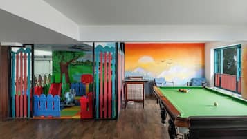 A room with a pool table, a green felt table, and a mural depicting a sunset over mountains.