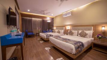 A hotel room with two beds, a desk, a chair, a TV, and an air conditioning unit.