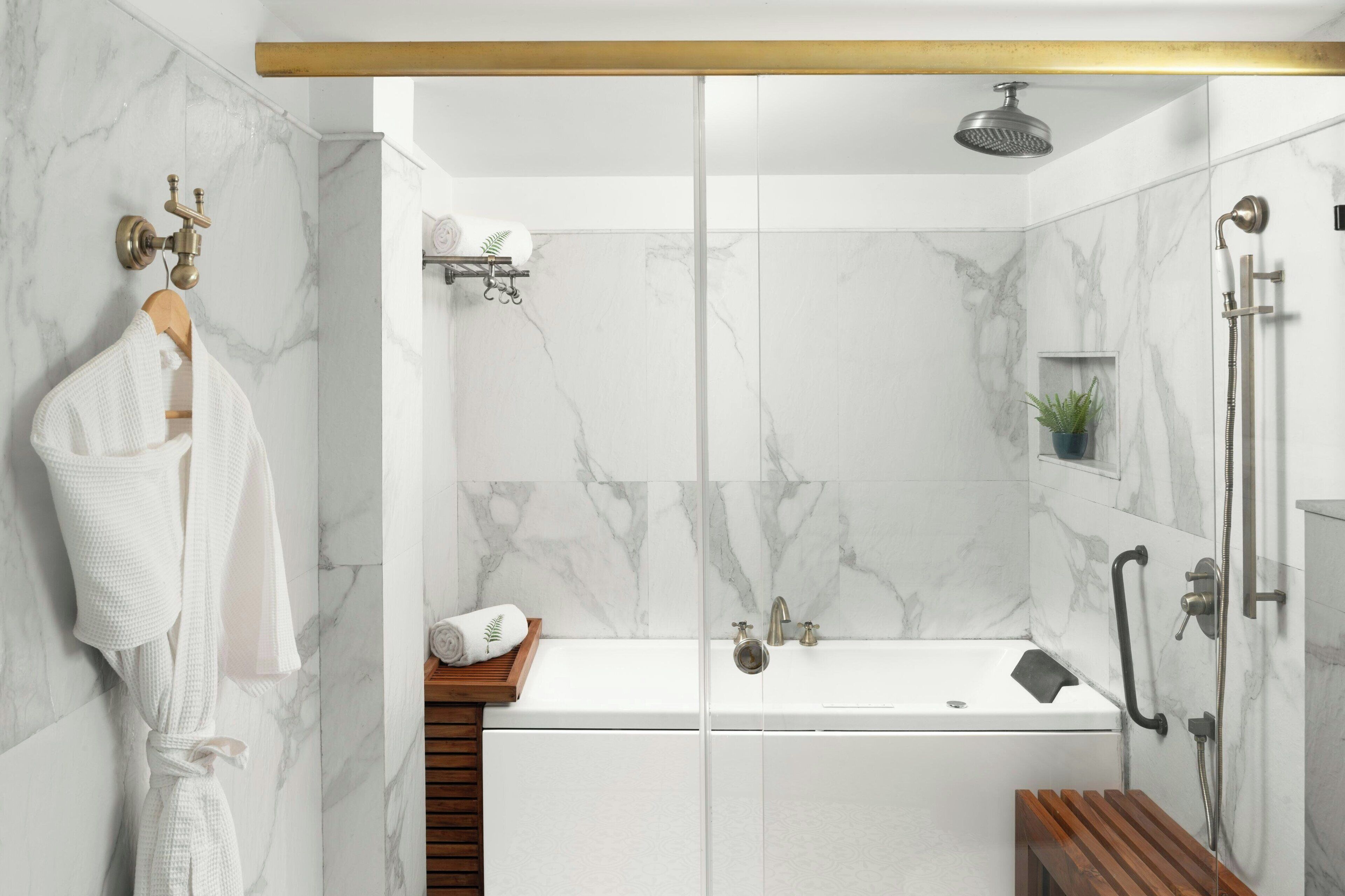 A modern bathroom with a glass-enclosed shower, a white bathtub, and a wooden bench.