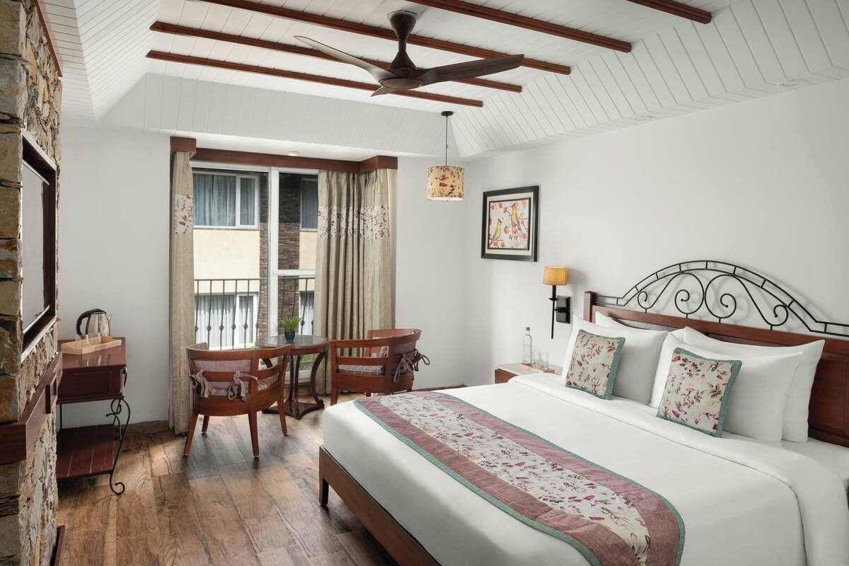 A hotel room with a large bed, wooden furniture, a ceiling fan, and a window with curtains.