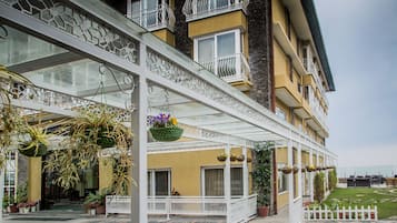 A hotel with a covered outdoor area featuring a patterned floor, hanging planters with flowers, and a white fence.