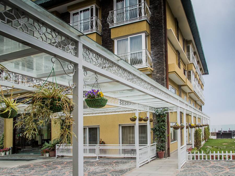 A hotel with a covered outdoor area featuring a patterned floor, hanging planters with flowers, and a white fence.