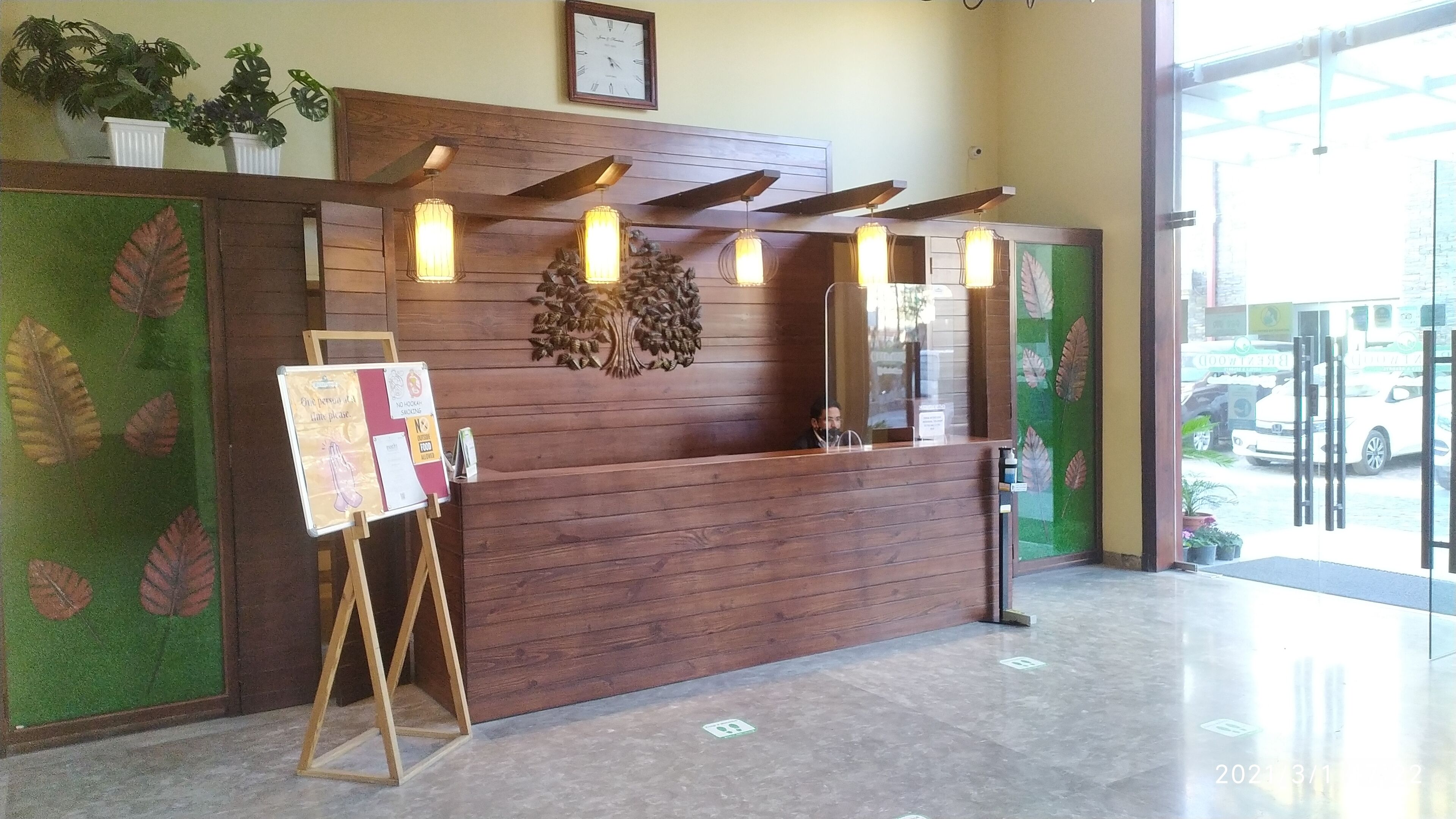 A reception desk with a wooden finish, a bulletin board, and a large window with a view of parked cars outside.