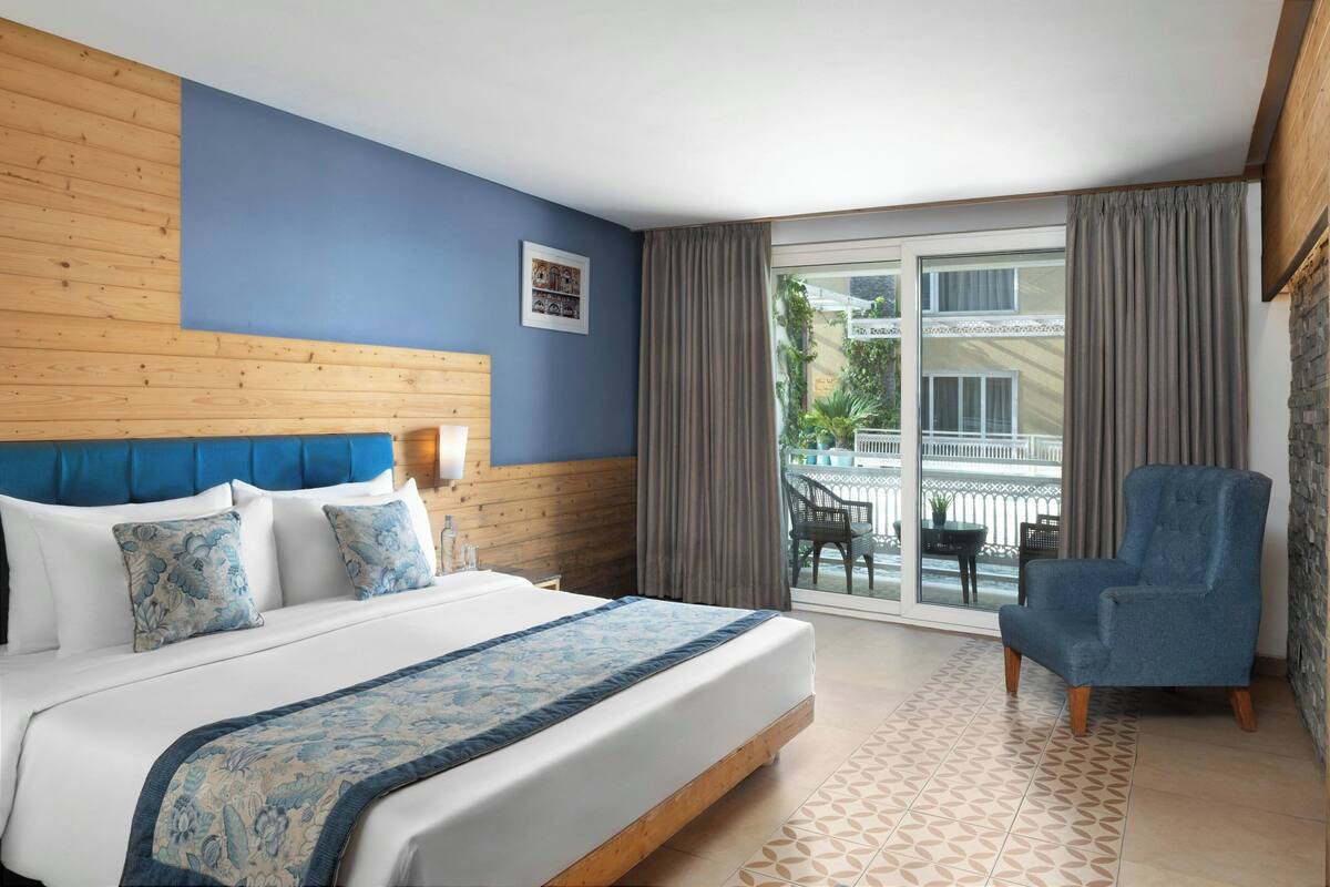A hotel room with a bed, a chair, a window, and a view of the outside.