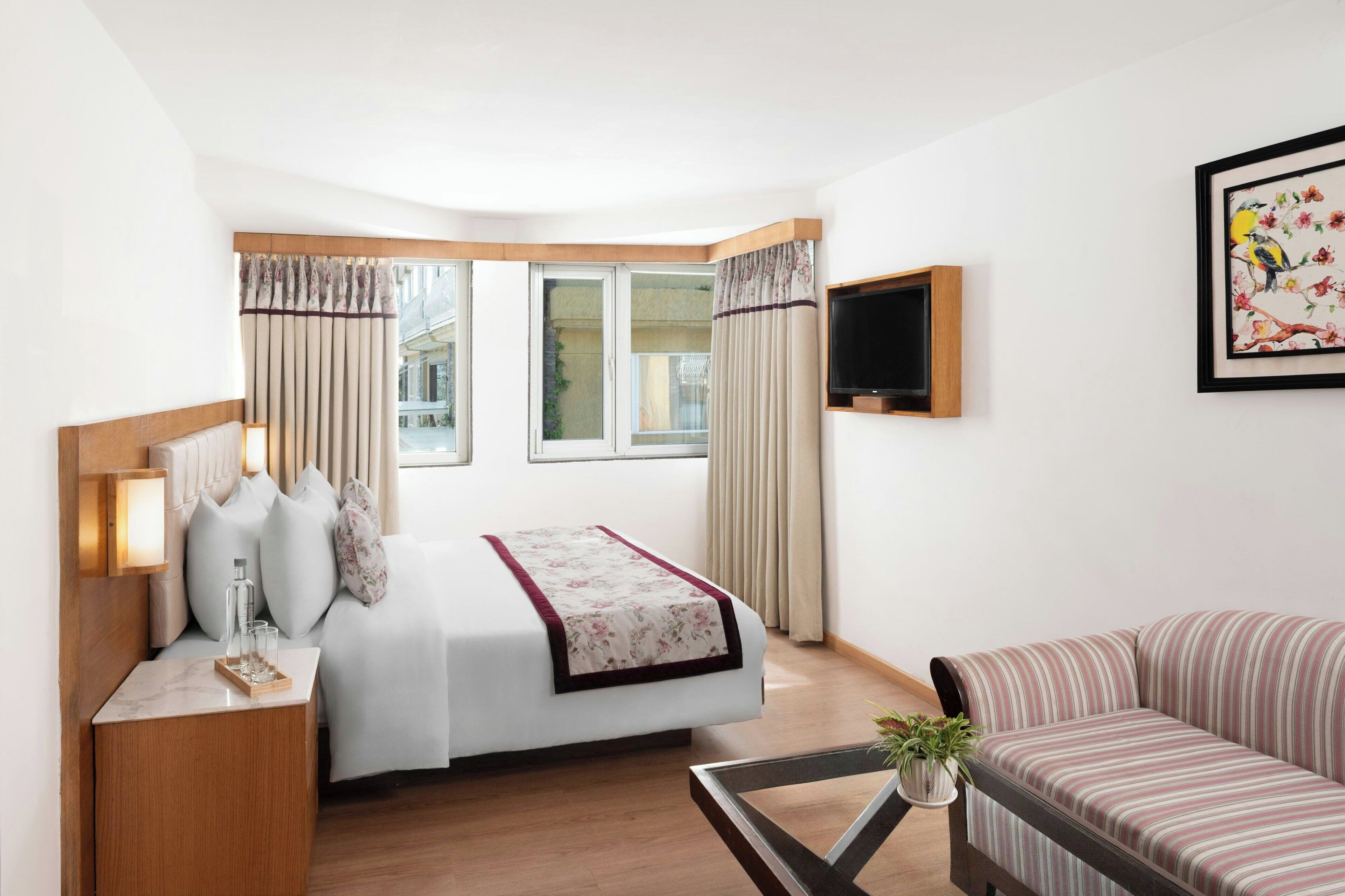 Una habitación de hotel con cama, mesita de noche, lámpara, televisión y sofá.